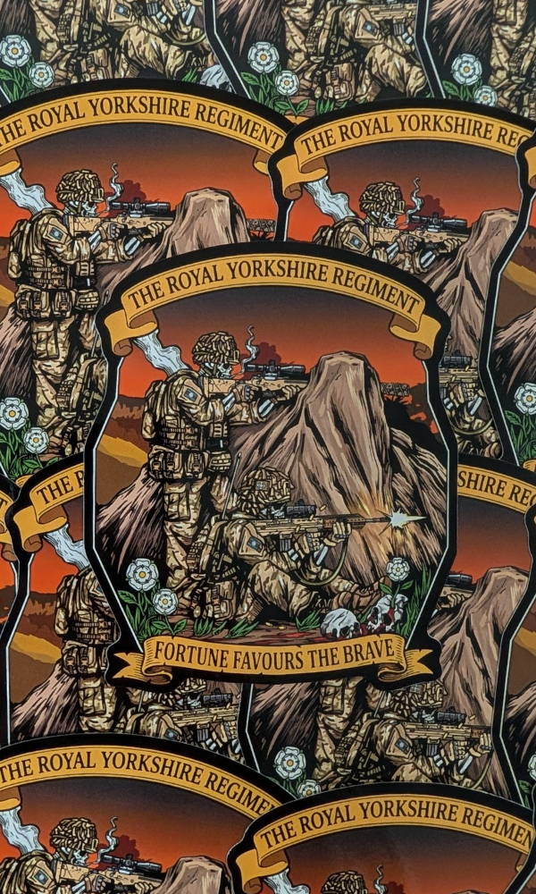 A close-up of a repeating printed design featuring illustrated soldiers, rocky terrain, and banners reading 'THE ROYAL YORKSHIRE REGIMENT' and 'FORTUNE FAVOURS THE BRAVE.' This appears to be the product surface itself rather than a lifestyle scene, so subject_type is Product by Mora Tactical.